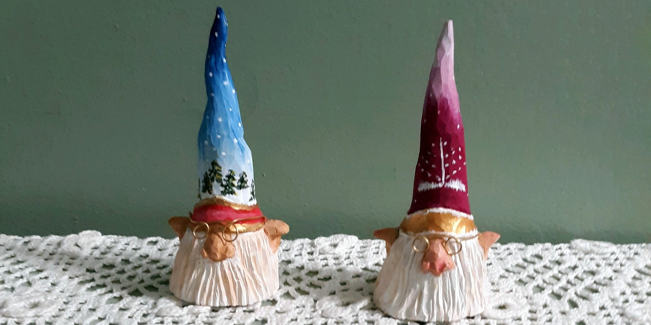 two carved wooden gnome-like faces under tall pointed and painted hats with winter motifs