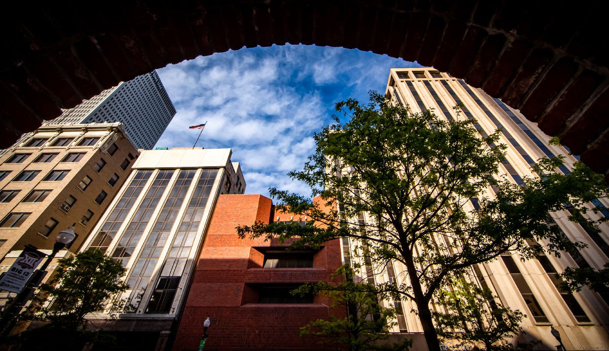 City buildings viewed from beneath an archway, with a semicircle of blue sky above them.