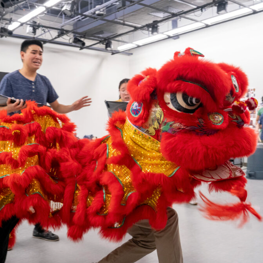 actors in rehearsal interact with a red Chinese dragon costume