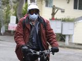 A man wearing a mask and goggles rides his bike out of the parking lot at the Life Care Center is shown in Kirkland, Wash., near Seattle, Tuesday, March 3, 2020. The facility has been tied to several confirmed cases of the COVID-19 coronavirus. (AP Photo/Ted S. Warren)