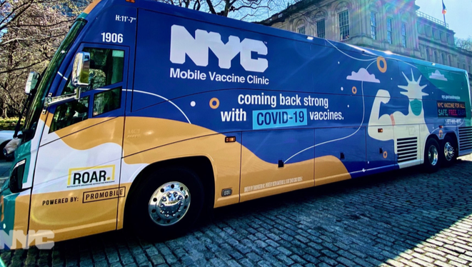 Image of large passenger bus covered in blue yellow and white designs that say NYC Mobile Vaccine Clinic