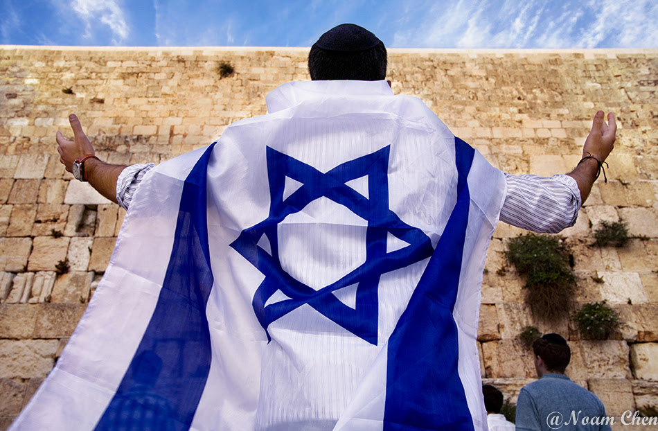 man wearing the flag of israel and raises his hands at the western wall, jerusalem