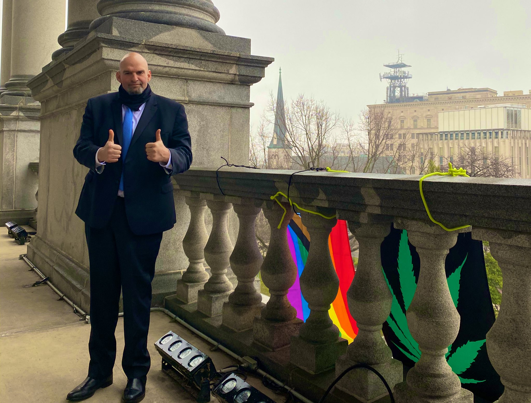 John Fetterman stands in front of pride and weed flags.