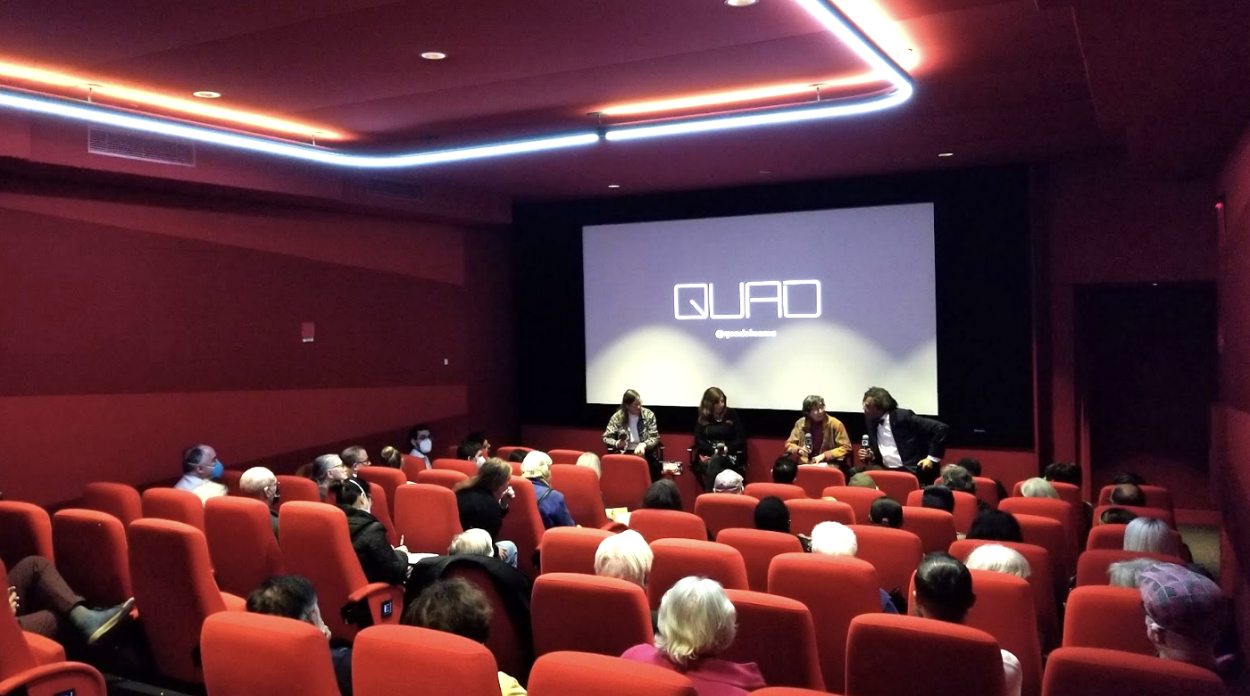 Photograph of panel of four people sitting in the front of a very

red movie theater screening room.