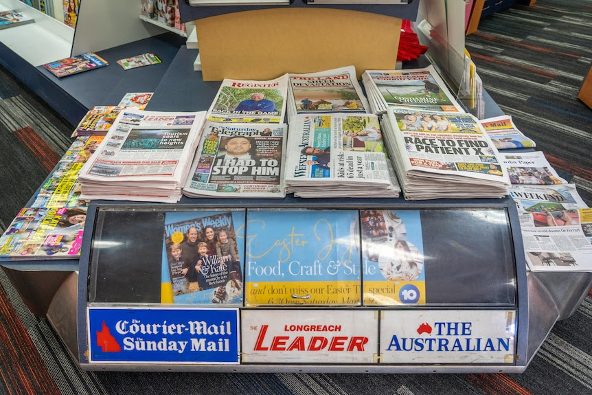 Stacks of newspapers sit on a display in a newsagency.