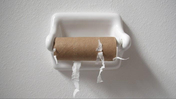 Empty toilet paper roll on the holder with a plain white wall background.