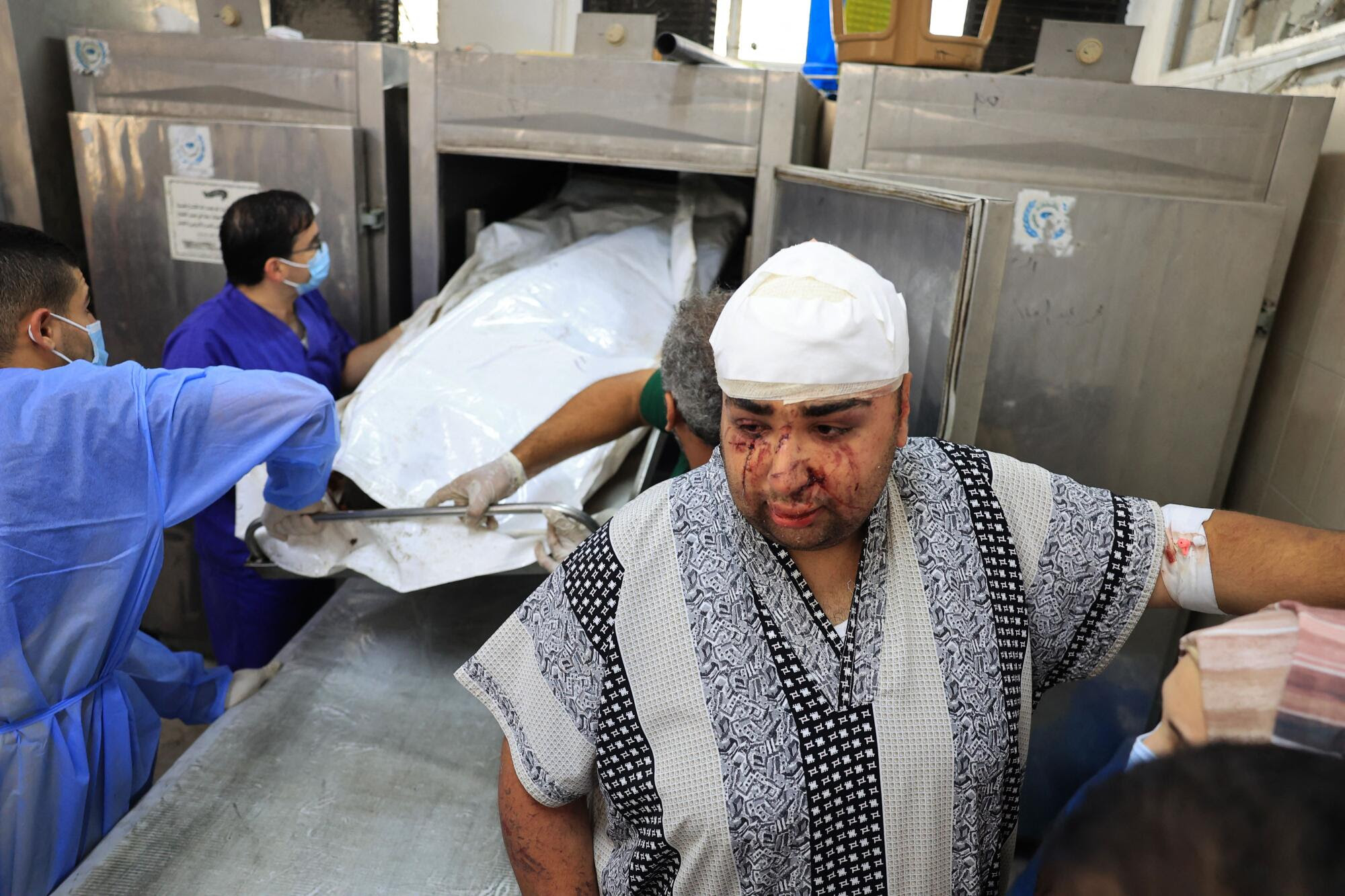 Un hombre herido observa mientras sacan un cuerpo del refrigerador de la morgue de un hospital.