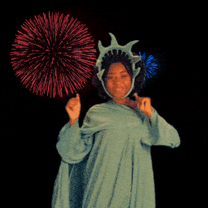 Image of a woman in a Statue of Liberty costume dancing in front of fireworks