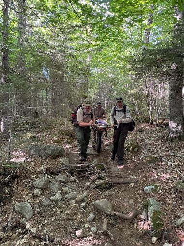 Rangers carrying injured hiker on wheeled litter down a trail in the woods