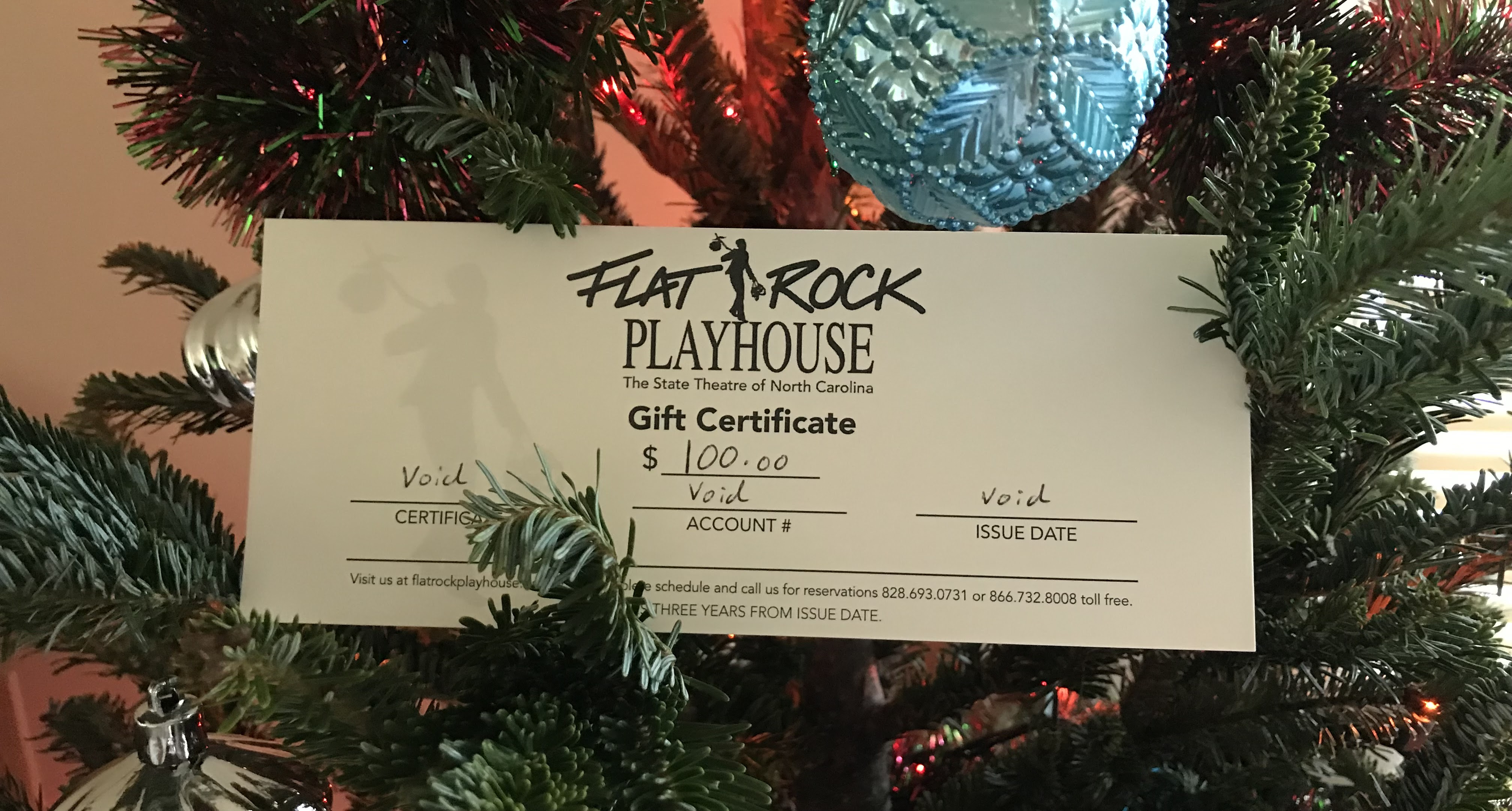 Flat Rock Playhouse Gift
                Certificate sits on a decorated Christmas tree