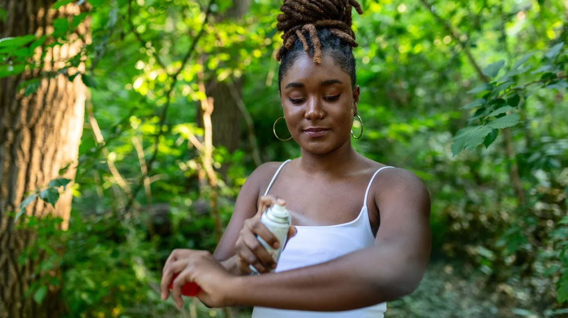 A woman spraying insect repellent in her arm.