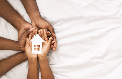 Family holds hands together with a small paper house in their palms. 