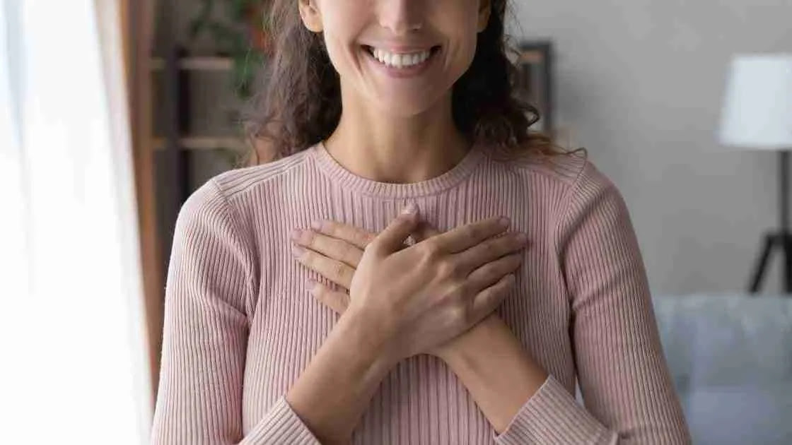 A smiling woman crosses her hands over her heart.