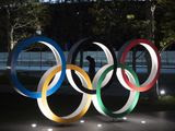 A man is seen through the Olympic rings in front of the New National Stadium in Tokyo, Tuesday, March 24, 2020. IOC President Thomas Bach has agreed &quot;100%&quot; to a proposal of postponing the Tokyo Olympics for about one year until 2021 because of the coronavirus outbreak, Japanese Prime Minister Shinzo Abe said Tuesday. (AP Photo/Jae C. Hong)