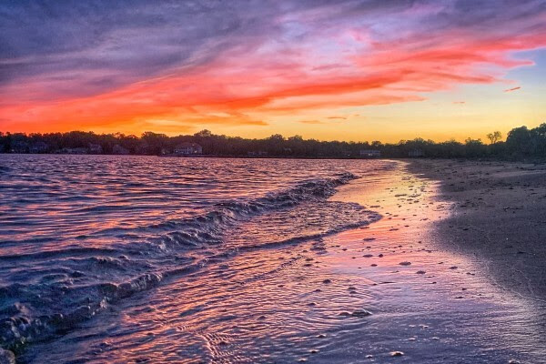 Late evening clouds cast a rainbow of colors on a quiet shoreline.