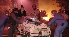 Doctors and nurses evacuating patient in bed from hospital with fire in background