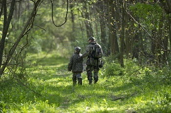 Spring turkey hunt, a view of an adult and child, dressed in hunter camouflage, walking away down a forested trail