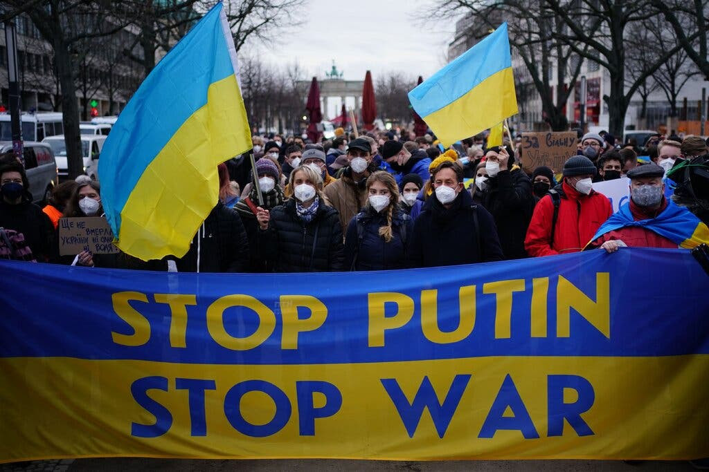 A crowd holds Ukrainian flags and a sign denouncing Russian President Vladimir Putin.