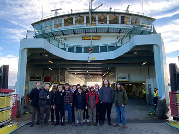 Several people posing for a photo in front of a ferry docked at a terminal