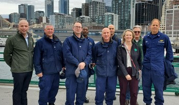 Photo of group of people on outdoor deck of ferry with Seattle skyline in the background