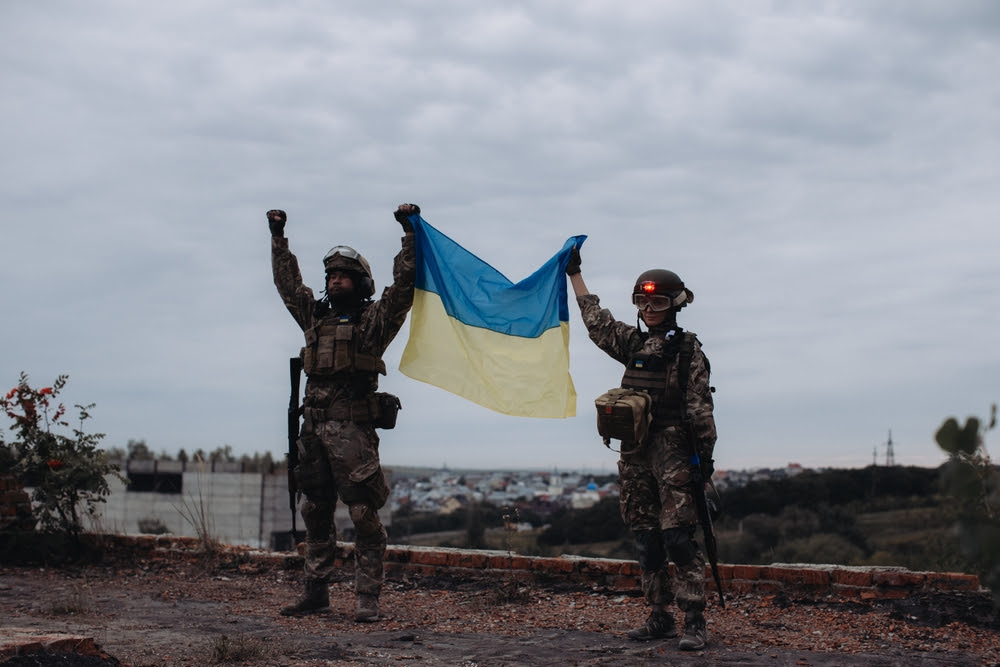 Two soldiers stand holding a Ukrainian flag high