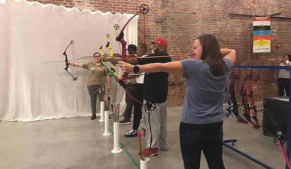 row of people aiming bows and arrows during archery class