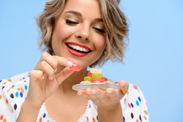 Portrait of young beautiful woman with sweets over blue wall