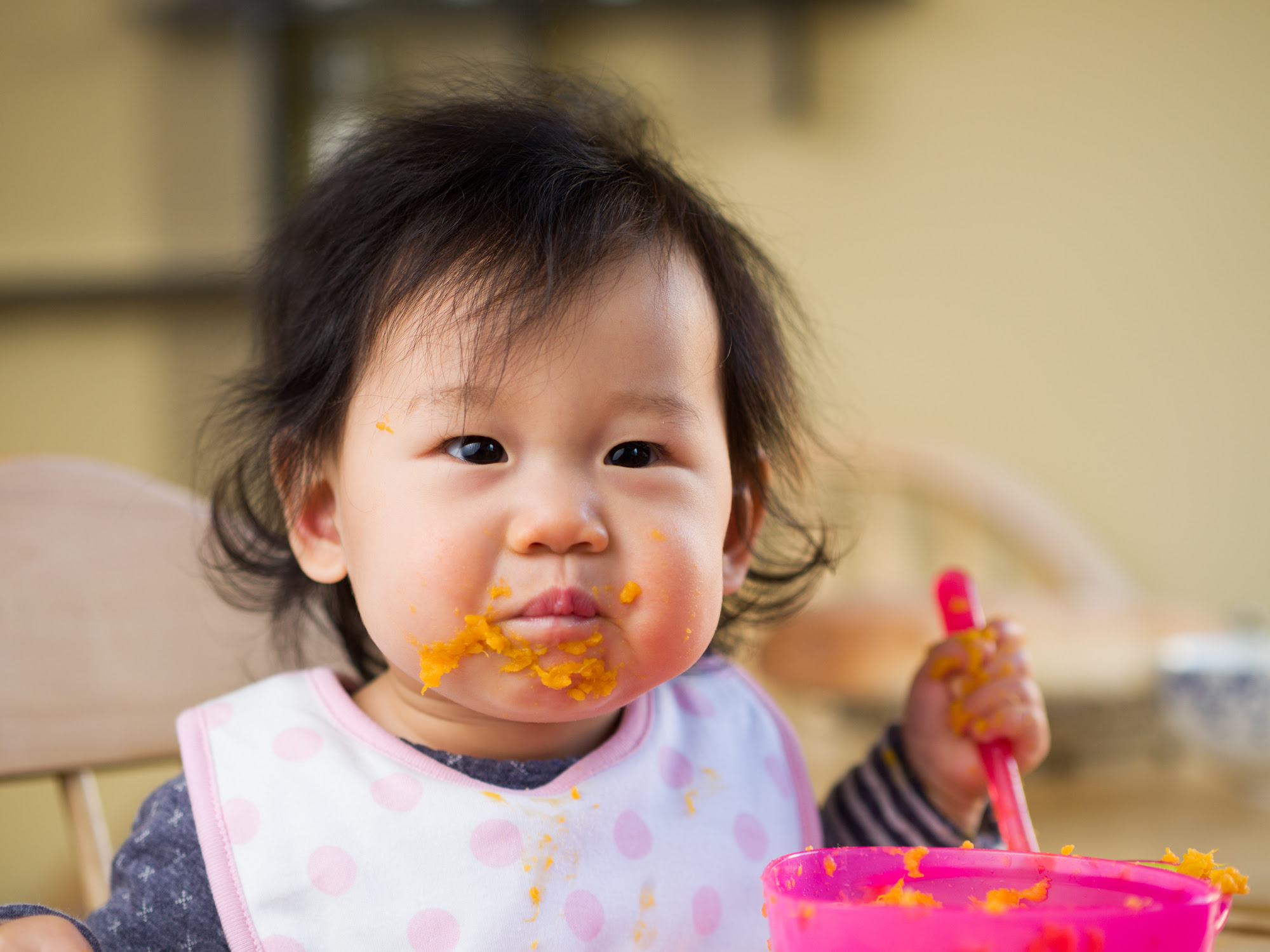 Toddler eating mushed carrots from bowl. 