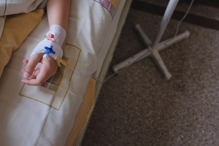 Child's hand resting on hospital bedsheet with IV drip attached