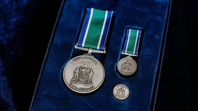A medallion, a medal and coin with the Order of Ottawa emblem sit on top of blue velvet in display box. 