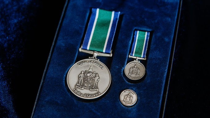 A medallion, a medal and coin with the Order of Ottawa emblem sit on top of blue velvet in display box.