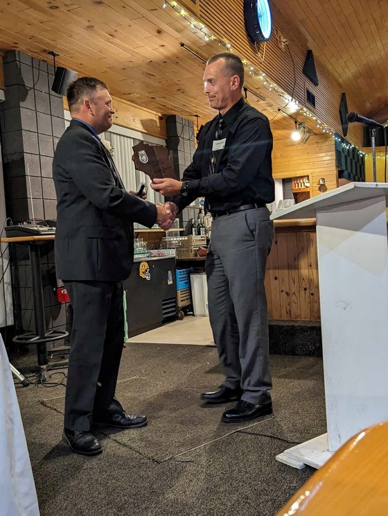 Lt. Lockman, wearing a dark suit, shakes hands with a supervisor as he receives his award. 